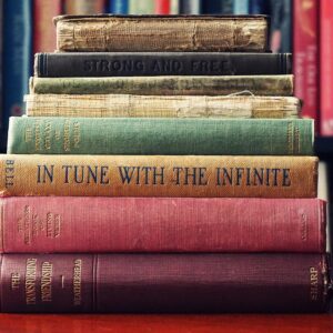 A stack of vintage hardcover books on a wooden table in a cozy library setting.