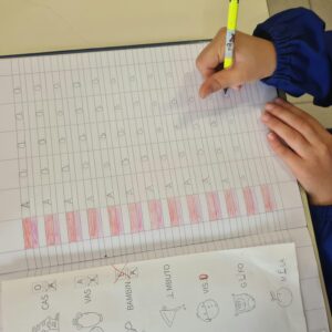 A child in a blue sleeve writes letters in a notebook for educational practice.