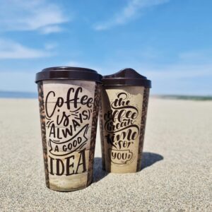 Stylish coffee cups on a sandy beach under a bright blue sky.