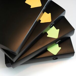 A stack of black ring binders with yellow and green labels for organization.