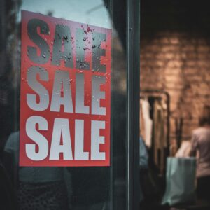 Red sale sign on a glass door with interior view of a clothing store.