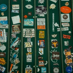 Vibrant collection of street art stickers on a green fence in Paris, showcasing urban subculture.