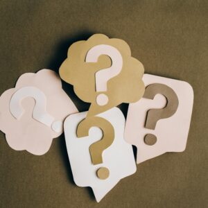 Four paper cutouts of question marks in beige and white on a brown surface, symbolizing inquiry and curiosity.