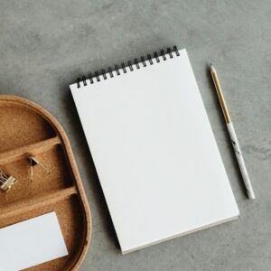 Flat lay of notepad, pencil, and binder clips on a grey surface, ideal for business mockups.