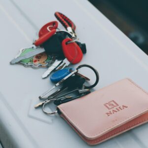 A set of keys with a cute keychain next to an elegant leather wallet on a white surface.